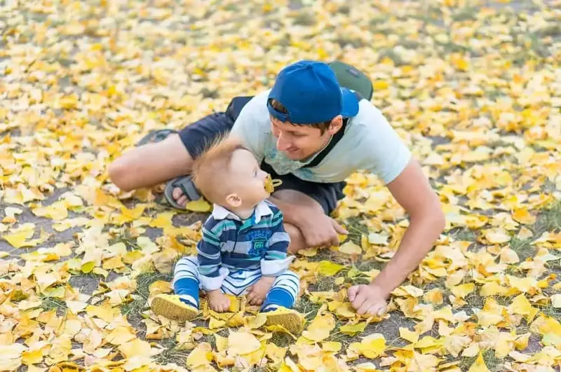 Toddler playing in leaves with his dad