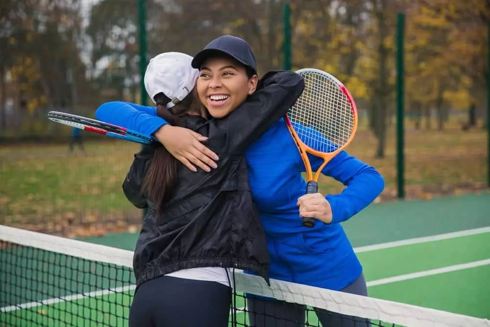 two girls hugging on tennis court
