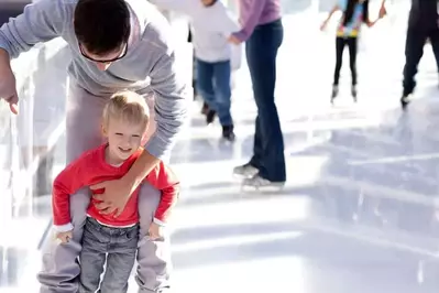 A little boy ice skating with his father.